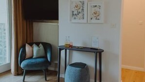 A modern living room with a blue armchair, a small table with a basket, and artwork on the wall. - Haggn&Co (Neukirchen)