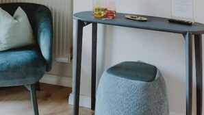 A room with a dark blue chair, a grey ottoman, a small table with drinks, and two framed floral artworks on the wall. - Haggn&Co (Neukirchen)