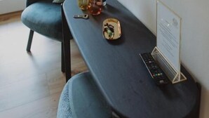 A modern room with a dark wooden table, a sofa with cushions, a TV mounted on the wall, and a window with curtains. - Haggn&Co (Neukirchen)
