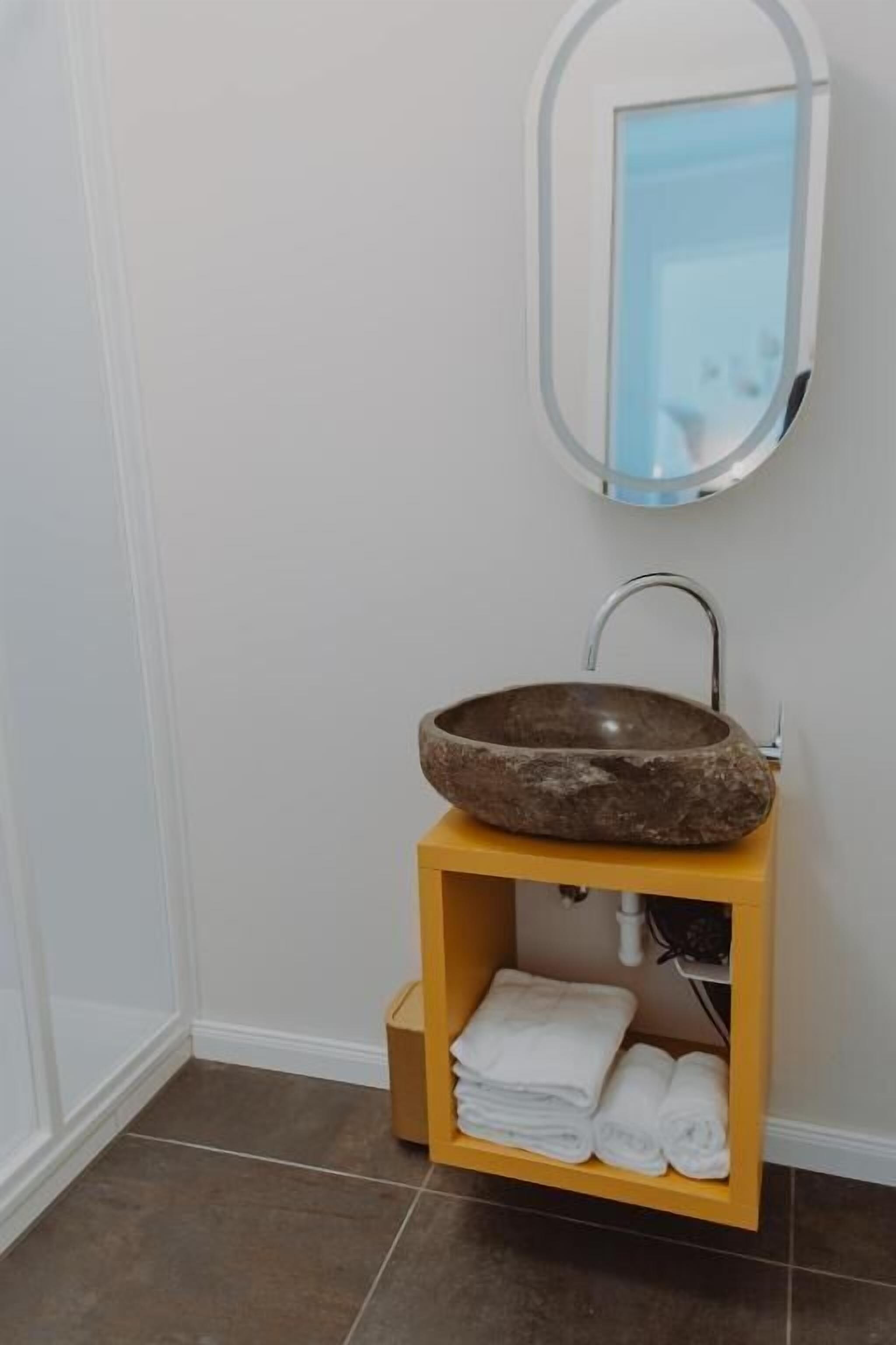 A bathroom with a stone sink, a mirror, and a shelf with folded towels.