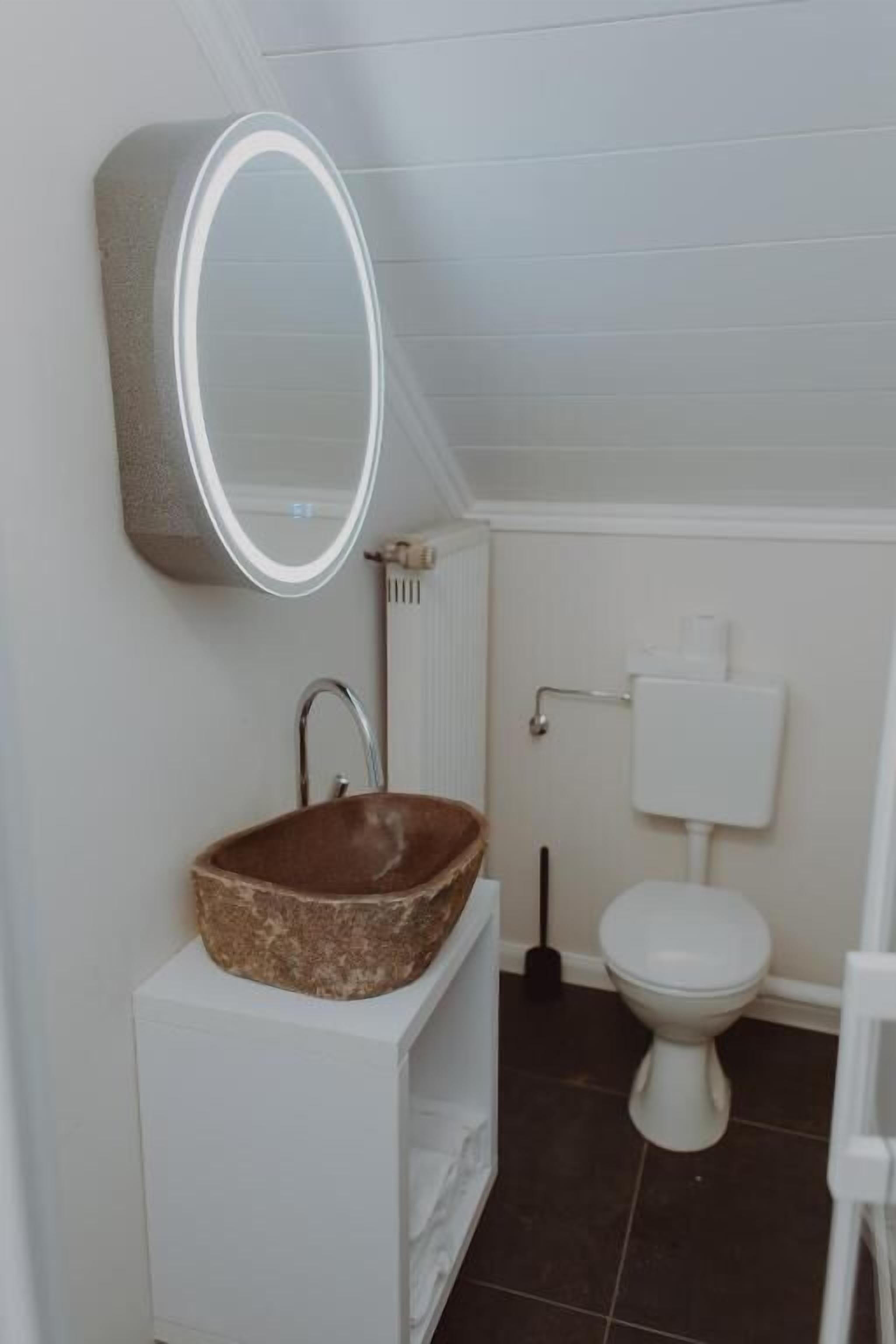 Un baño con un lavamanos blanco, un espejo redondo, un inodoro blanco y un radiador.