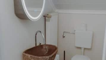 Un baño con un lavamanos blanco, un espejo redondo, un inodoro blanco y un radiador.