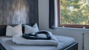 A modern bedroom with a bed, pillows, and a view of trees through a window.