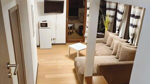 A living room with a sofa, a coffee table, a TV, and a refrigerator.