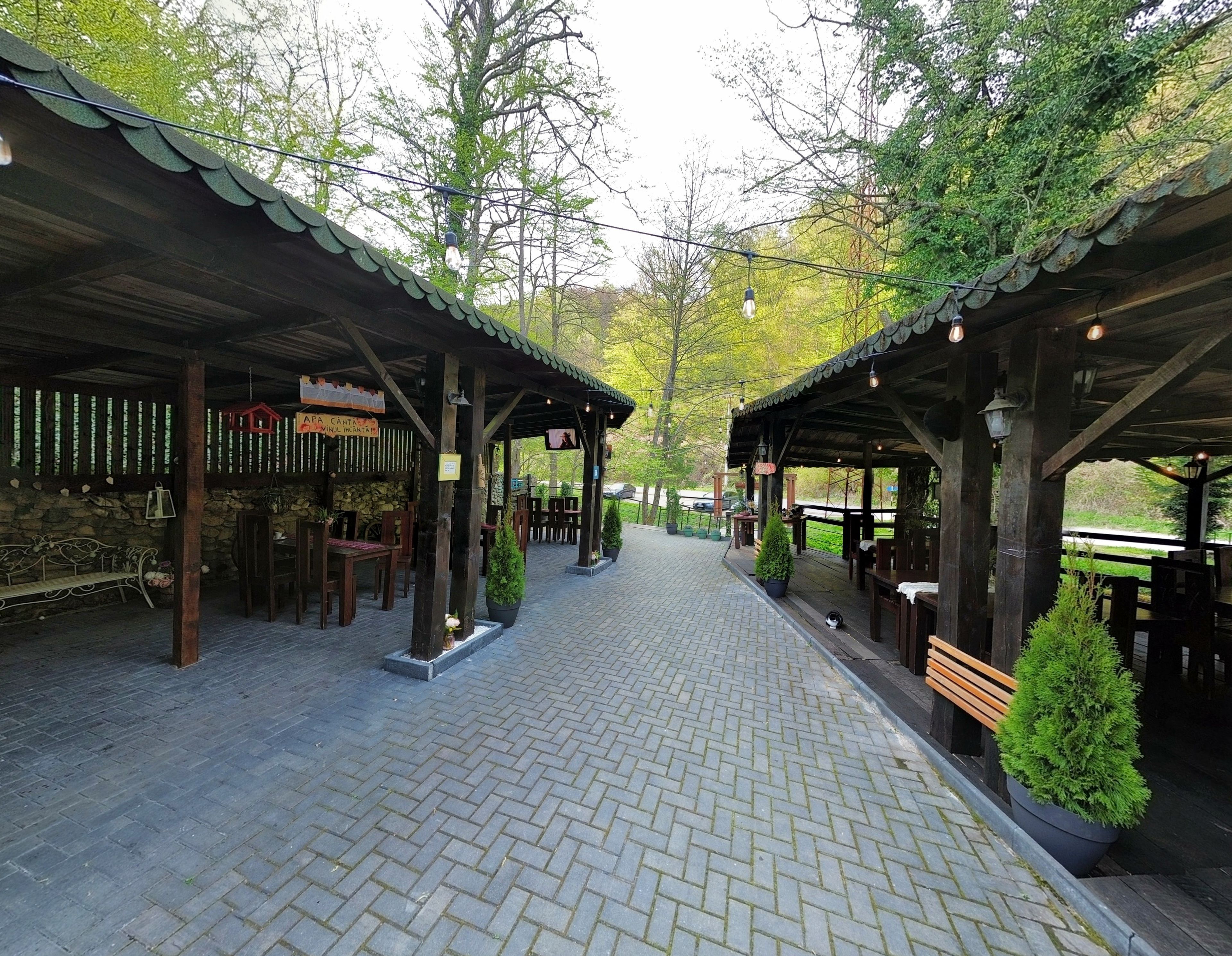 A covered outdoor seating area with stone walls, wooden benches, and potted plants.