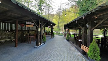 A covered outdoor seating area with stone walls, wooden benches, and potted plants.