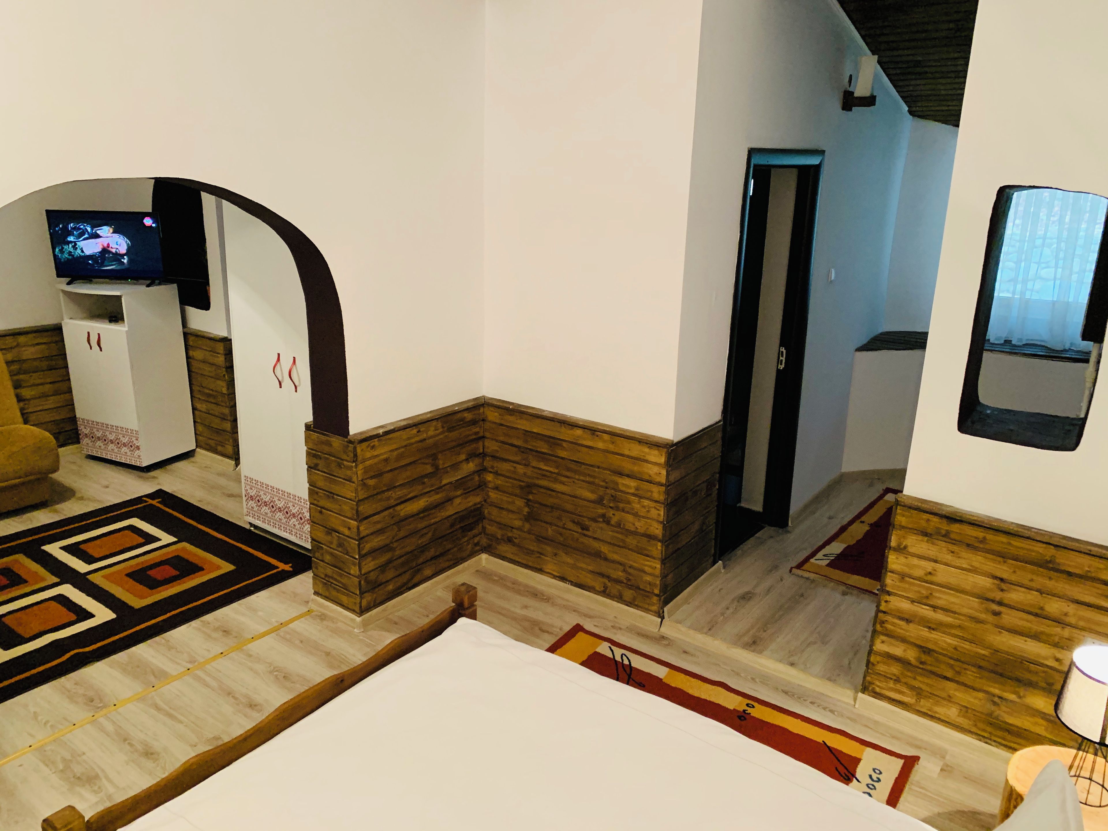 A room with a bed, a TV, a wooden accent wall, a door, and a window.