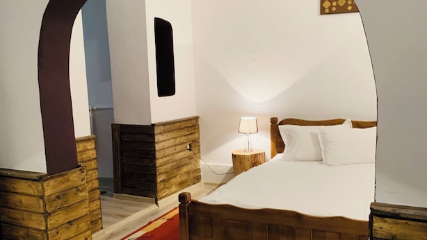 Un dormitorio con una cama de madera, una mesita de noche, una lámpara y un arco de madera.