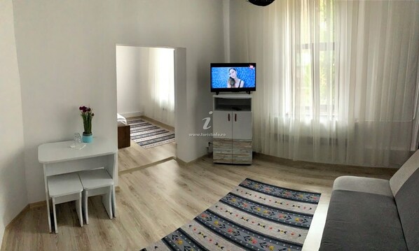 A modern living room with a television, a sofa, a dining table with chairs, and a decorative rug. - Vila Ursu- Tismana (Tismana)