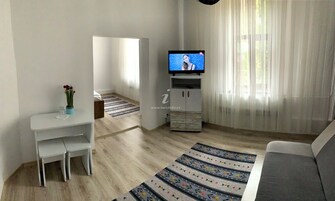 Una sala de estar moderna con televisor, un sofá, una mesa de comedor con sillas y una alfombra decorativa.