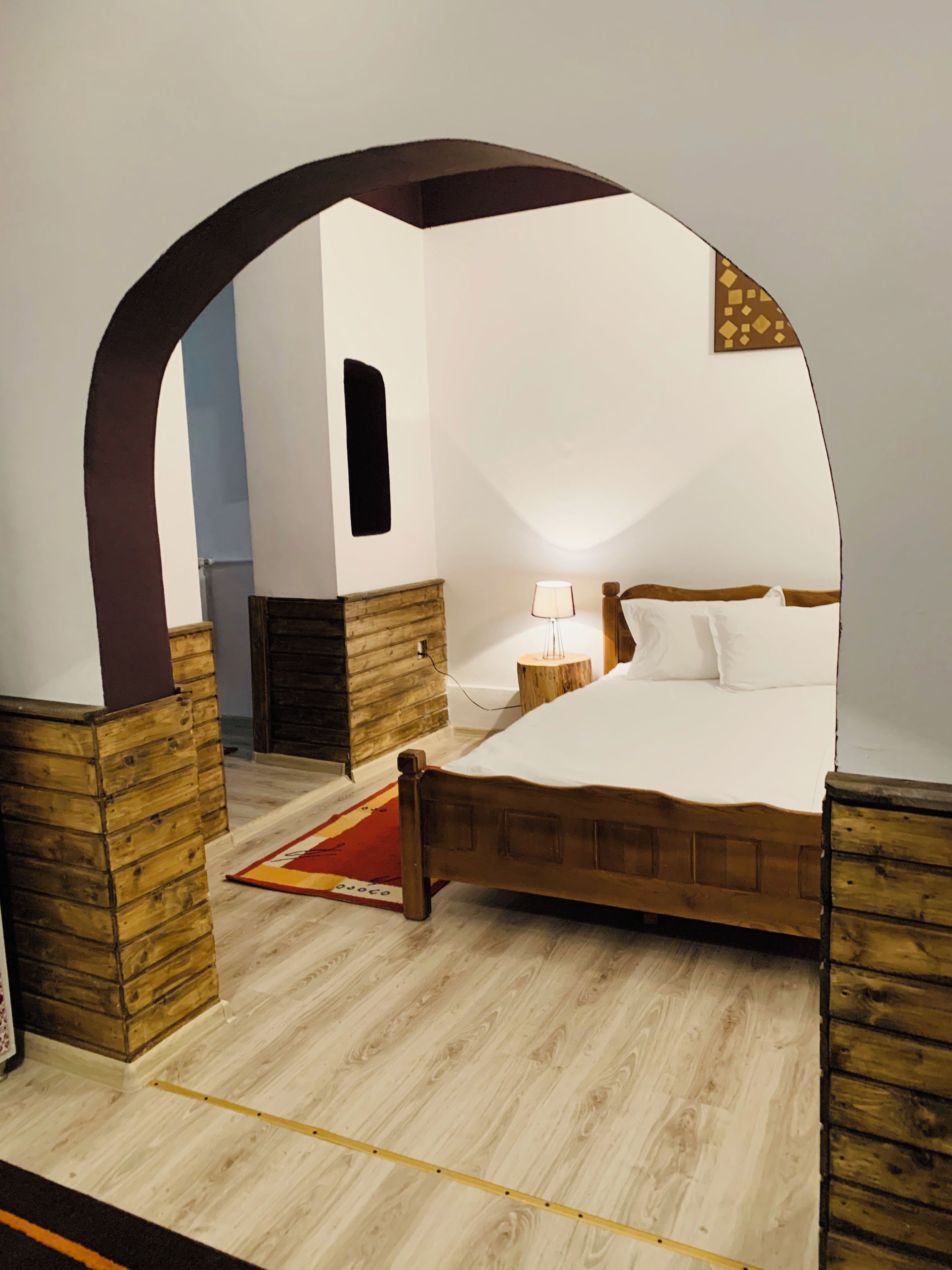 A bedroom with a wooden bed, a nightstand, a lamp, and a wooden archway.