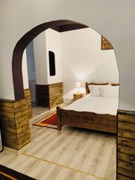 Un dormitorio con una cama de madera, una mesita de noche, una lámpara y un arco de madera.