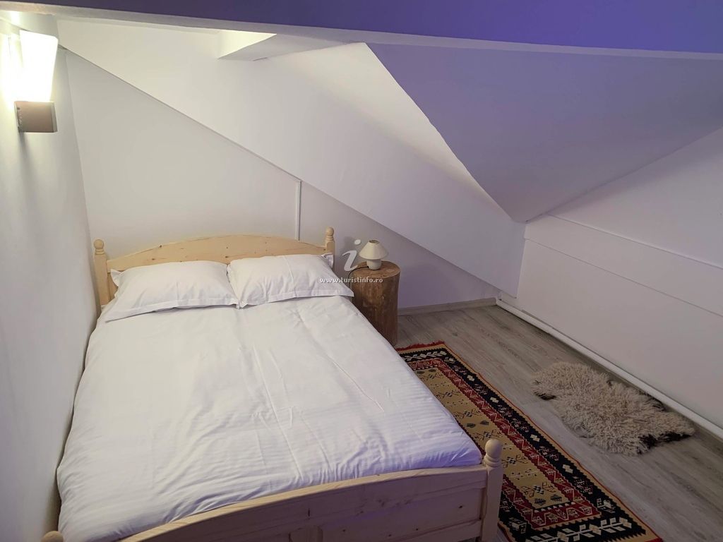 Un dormitorio con techo inclinado, una cama de madera, una mesita de noche con lámpara y una alfombra estampada.