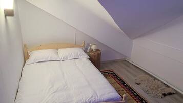 Un dormitorio con techo inclinado, una cama de madera, una mesita de noche con lámpara y una alfombra estampada.