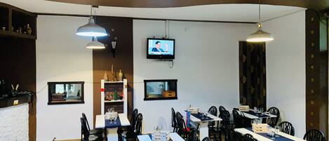 A restaurant with multiple tables and chairs, a television screen, and pendant lighting.