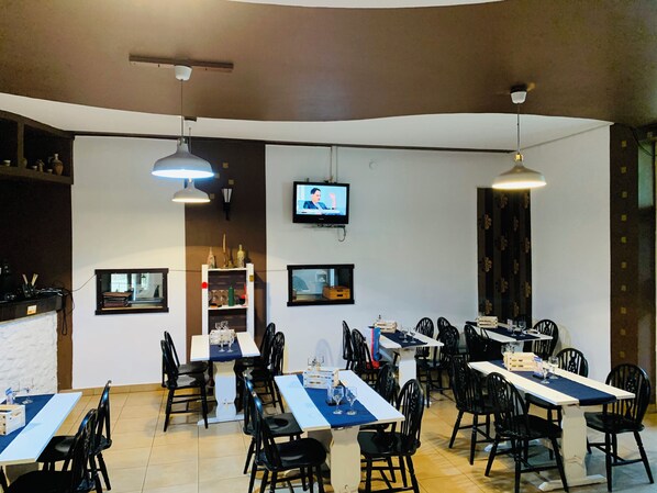 A restaurant with multiple tables and chairs, a television screen, and pendant lighting.