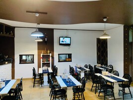 Un restaurante con varias mesas y sillas, una pantalla de televisión e iluminación colgante.