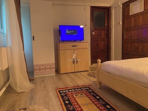 A bedroom with a wooden bed, a television on a wooden cabinet, and a patterned rug. - Vila Ursu- Tismana (Tismana)