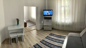 Una sala de estar moderna con televisor, un sofá, una mesa de comedor con sillas y una alfombra decorativa.