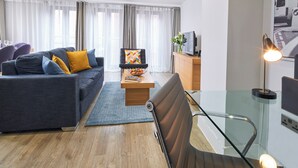 A modern living room with a grey sofa, a black chair, a wooden coffee table, and a glass staircase. - National at Tower Bridge (London)