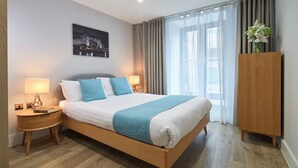 A hotel room with a large bed, wooden nightstands, a night lamp, a framed picture on the wall, and a wooden wardrobe. - National at Tower Bridge (London)