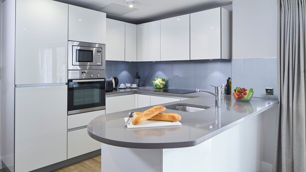 A modern kitchen with white cabinetry, a built-in microwave, a stainless steel oven, and a granite countertop. - National at Tower Bridge (London)