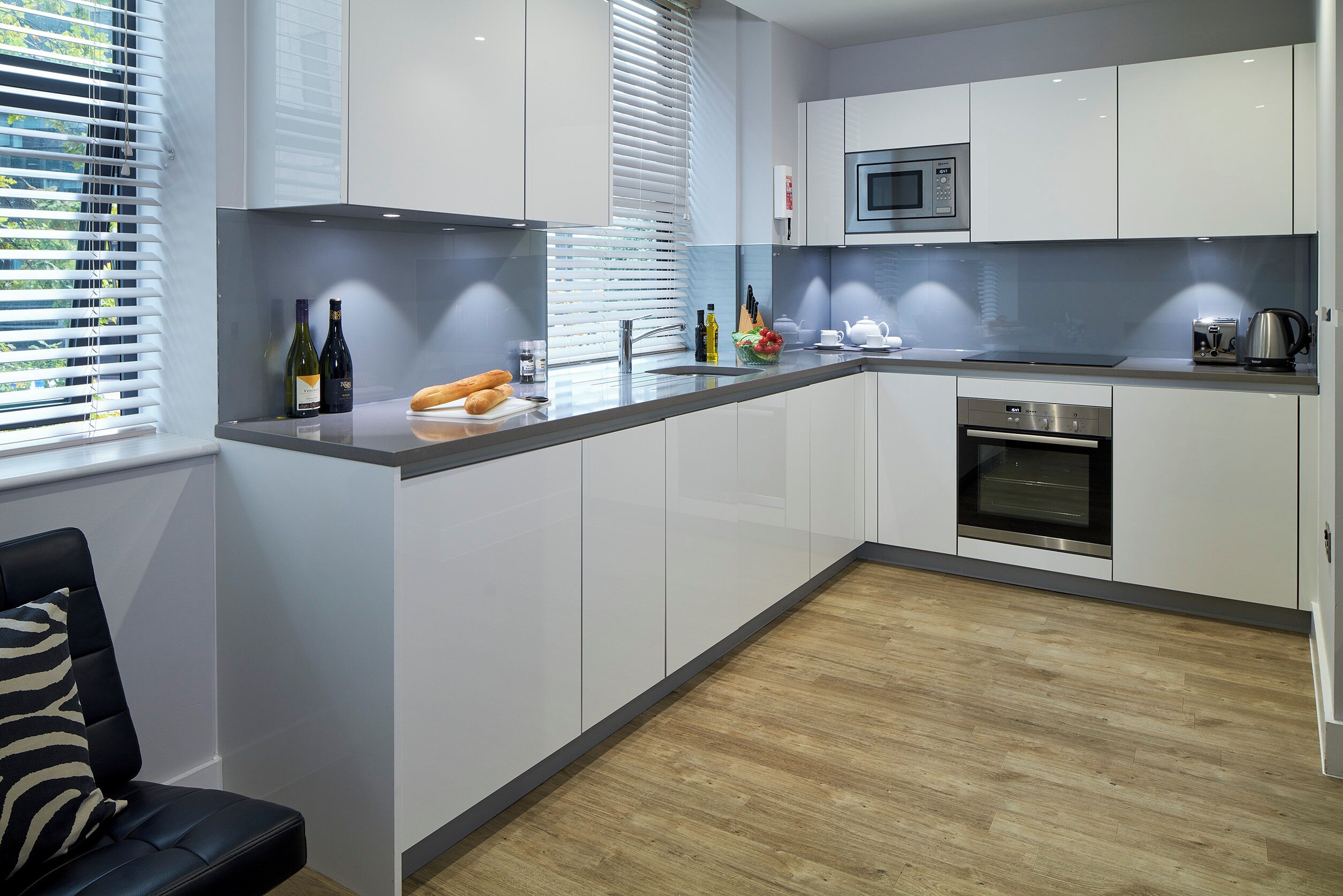 A modern kitchen with white cabinets, a built-in microwave, and a wooden floor.