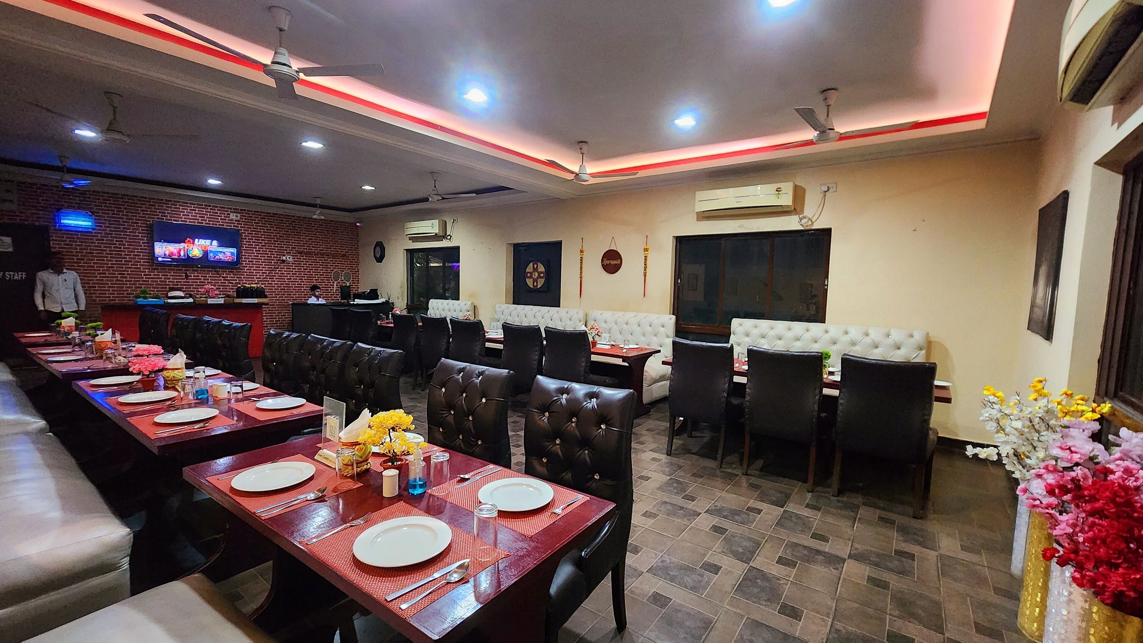 A restaurant with multiple dining tables, chairs, and a TV screen on the wall.