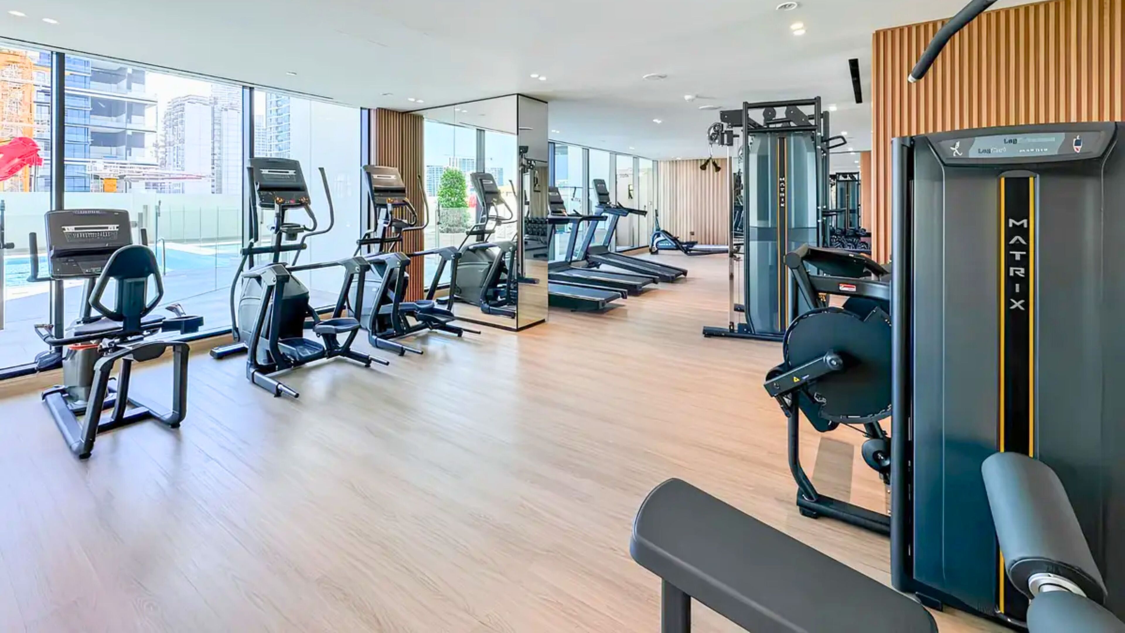 A modern gym with various cardio machines, weight training equipment, and a bench.