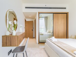 A modern hotel room with a wooden vanity, a large mirror, a bed with a white comforter, and a view of the city through a sliding glass door.
