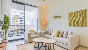 A modern living room with a sofa, two side tables, a potted plant, and a view of a cityscape through large windows. - Binghatti Lavender Residences- JVC (Dubai)
