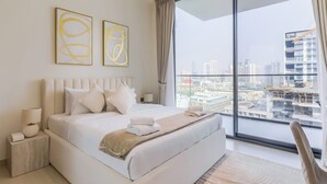 A modern hotel room with a large bed, a view of the city through floor-to-ceiling windows, and two abstract art pieces on the wall. - Binghatti Lavender Residences- JVC (Dubai)