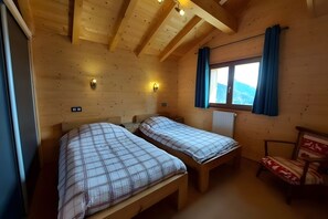 Een houten kamer met twee bedden, een stoel, een raam met gordijnen en wandlampen.