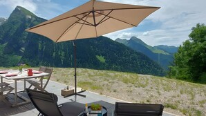 An outdoor dining area with a table, chairs, and a large umbrella, overlooking a mountainous landscape. - Morzine: panoramic, south-facing, comfortable chalet (Morzine)