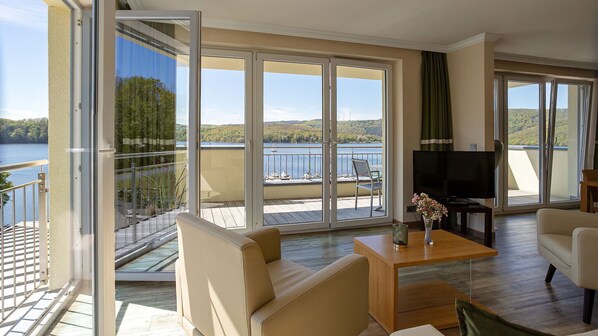 A spacious living area with a large sliding glass door leading to a balcony overlooking a lake.