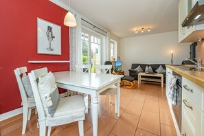 A modern kitchen with white cabinetry, a dining area with a white table and chairs, and a living area with a sofa and a TV. - Haus Conwind apartment 5a - Cozy vacation apartment with sauna, garden and (Sylt-Ost)