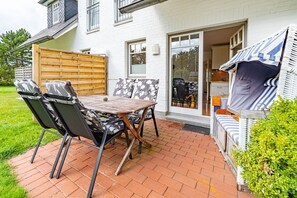 A patio with a table and chairs, a wooden fence, and a covered seating area with cushions.
