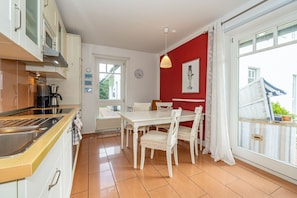 A modern kitchen with a dining area, featuring a white table and chairs, a red accent wall, and large windows.