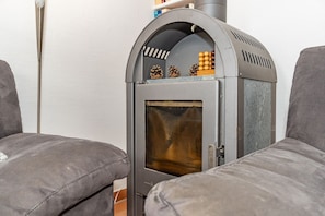 A wood-burning stove with a glass door, pine cones, and a small decorative item on top.