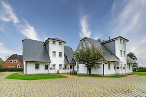 A row of white two-story houses with grey roofs, a paved driveway, and a tree in the foreground. - Haus Conwind apartment 5a - Cozy vacation apartment with sauna, garden and (Sylt-Ost)