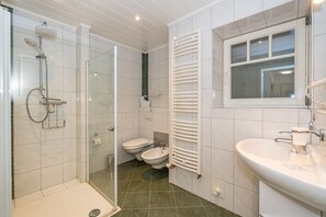 A bathroom with a glass-enclosed shower, two toilets, a sink, and a towel rack.