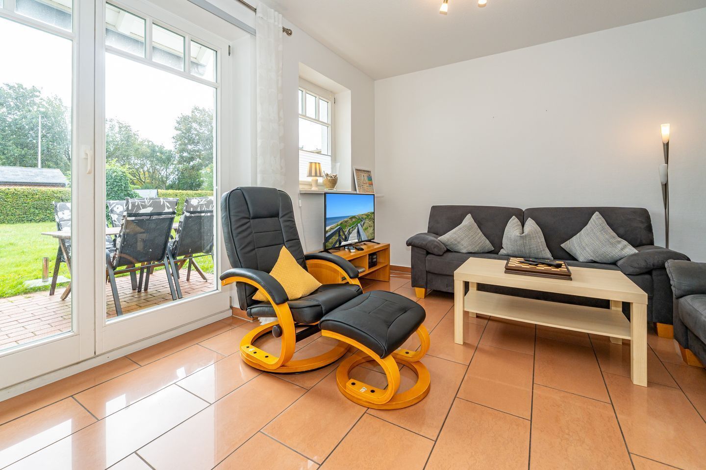 A spacious living room with a black leather chair, a grey sofa, and a wooden coffee table.