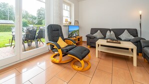 A spacious living room with a black leather chair, a grey sofa, and a wooden coffee table.