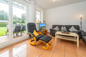 A spacious living room with a black leather chair, a grey sofa, and a wooden coffee table. - Haus Conwind apartment 5a - Cozy vacation apartment with sauna, garden and (Sylt-Ost)