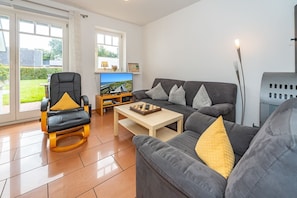A modern living room with a sofa, armchair, and a coffee table. There is a television and a chessboard on the coffee table.
