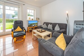 A modern living room with a sofa, armchair, and a coffee table. There is a television and a chessboard on the coffee table. - Haus Conwind apartment 5a - Cozy vacation apartment with sauna, garden and (Sylt-Ost)