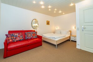 Une pièce avec un canapé en cuir rouge, un lit avec une literie blanche, un miroir rond avec une lampe et un petit tableau accroché au mur.
