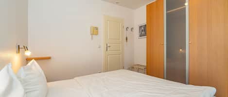 Ein Schlafzimmer mit Bett, Nachttischlampe, Kleiderschrank und einer Tür mit Lichtschalter.