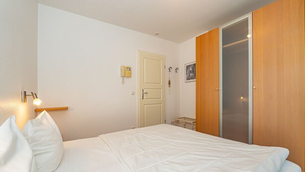 A bedroom with a bed, a bedside lamp, a wardrobe, and a door with a light switch.