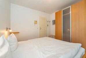 A bedroom with a bed, a bedside lamp, a wardrobe, and a door with a light switch.